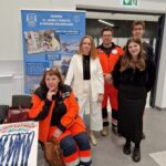 Grupa przedstawicieli Akademii im. Jakuba z Paradyża przy stoisku Wydziału Nauk o Zdrowiu. W tle roll-up promujący kierunki „Analityka medyczna” i „Dietetyka”. Osoby w strojach ratowniczych i reprezentacyjnych ubraniach promują ofertę edukacyjną.