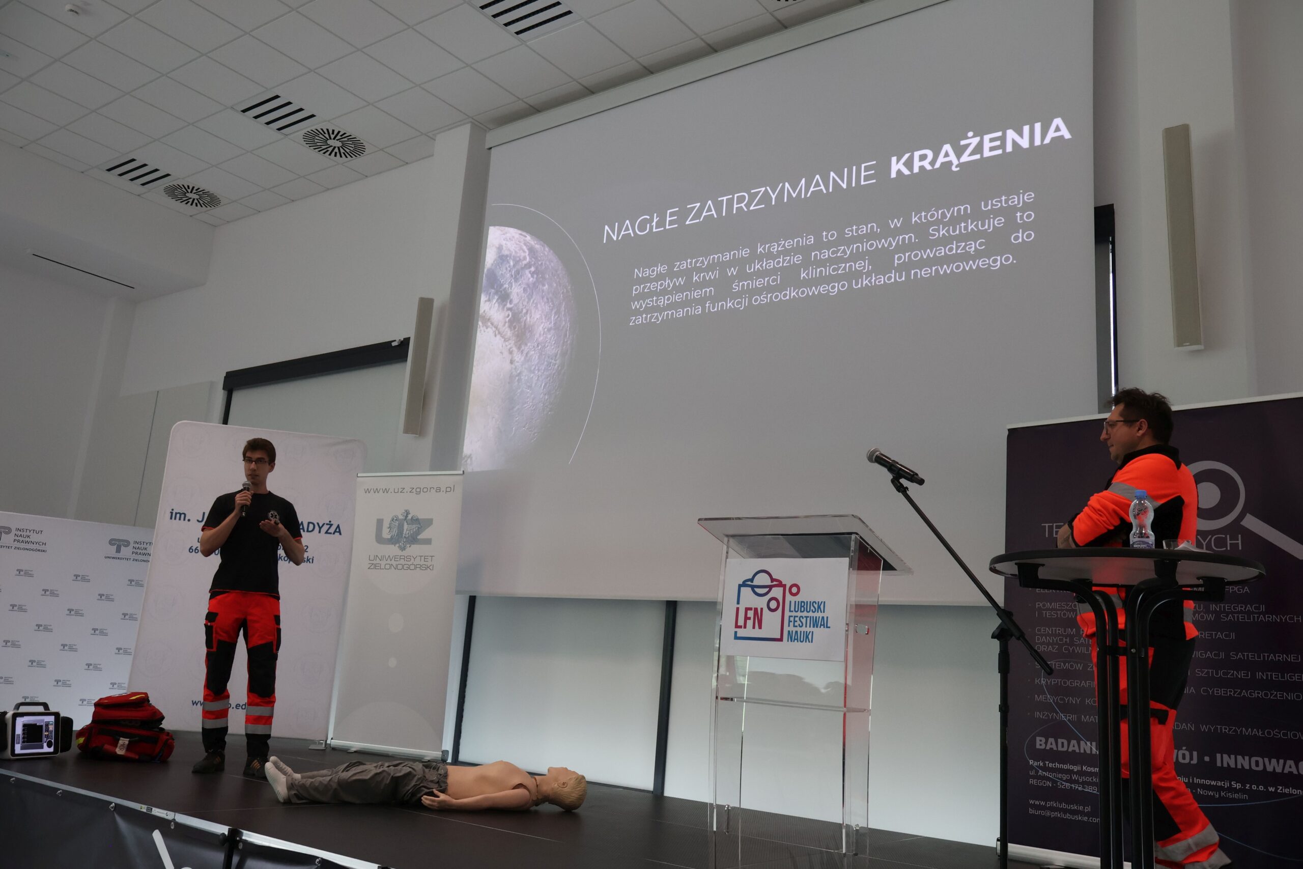 Prezentacja studentów ratownictwa medycznego Akademii im. Jakuba z Paradyża. Na scenie slajd poświęcony nagłemu zatrzymaniu krążenia, student omawia temat z mikrofonem w ręku. Obok manekin, sprzęt medyczny i prowadzący zajęcia.
