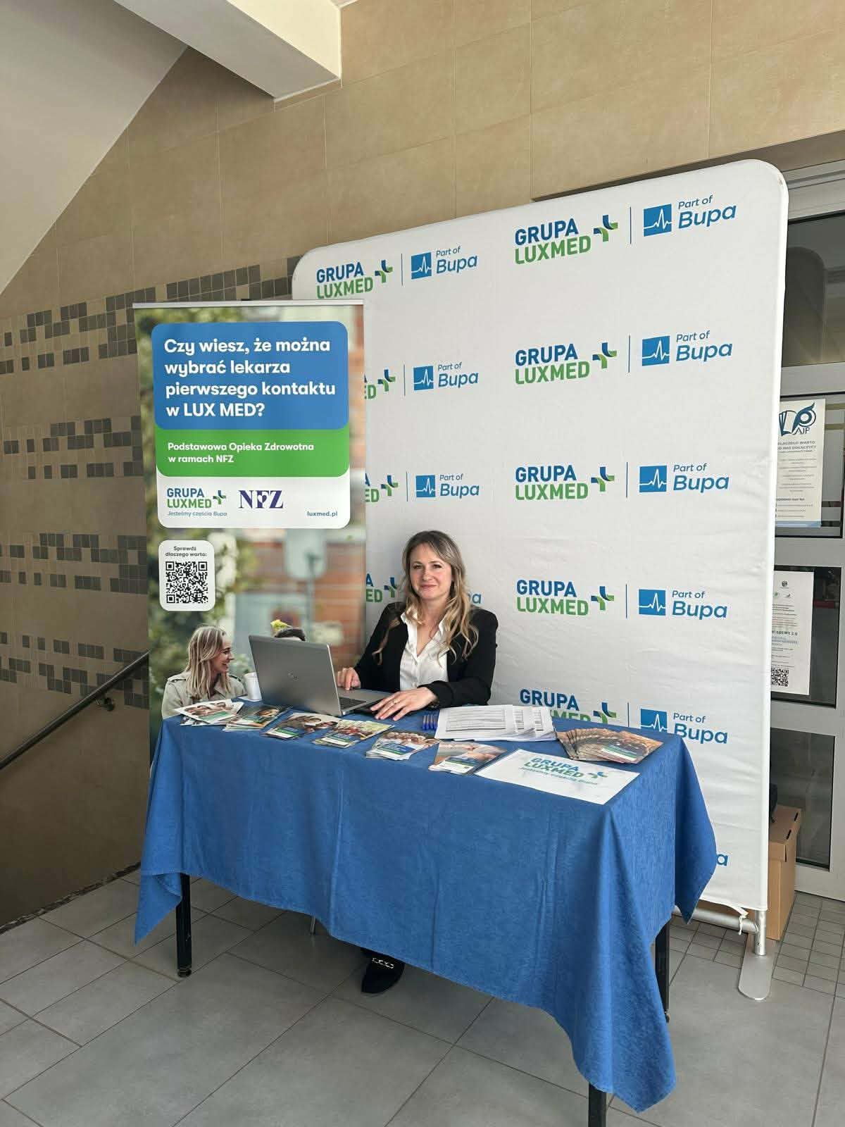 Stoisko informacyjne Grupy LUX MED, przy którym kobieta siedzi za laptopem i rozdaje materiały promujące wybór lekarza pierwszego kontaktu.