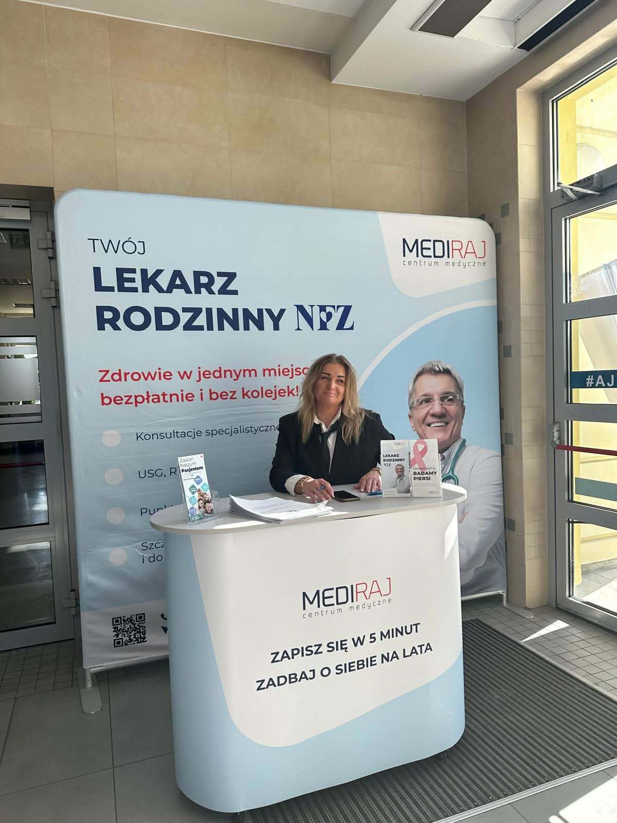 Stoisko MEDIRAJ z hasłem „Twój lekarz rodzinny NFZ”, gdzie kobieta siedzi za ladą i udziela informacji o usługach medycznych.